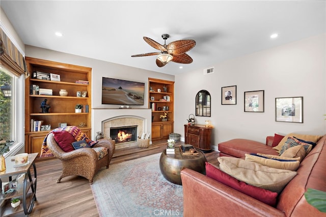 living room featuring ceiling fan, light wood-type flooring, and a tile fireplace