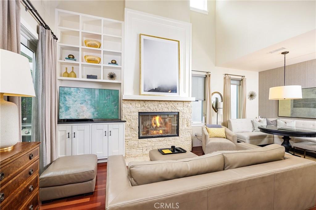 living room with dark hardwood / wood-style floors, a healthy amount of sunlight, a towering ceiling, and a fireplace