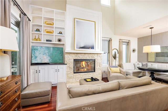 living room with dark hardwood / wood-style floors, a healthy amount of sunlight, a towering ceiling, and a fireplace