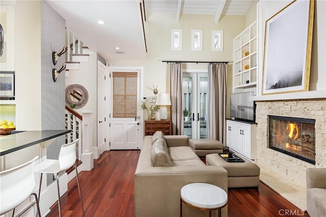 living room with beam ceiling, a stone fireplace, wood ceiling, and dark wood-type flooring