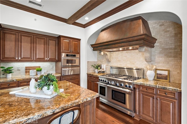 kitchen featuring premium range hood, backsplash, dark wood-type flooring, appliances with stainless steel finishes, and light stone counters