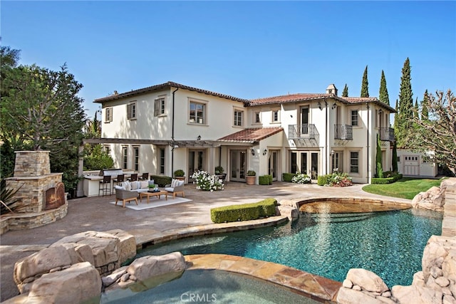 rear view of property with an outdoor living space with a fireplace, a balcony, and a patio