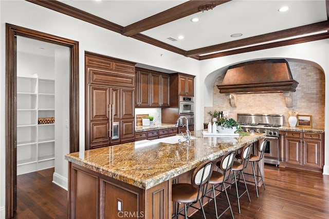 kitchen featuring light stone counters, custom exhaust hood, premium appliances, a center island with sink, and dark hardwood / wood-style floors