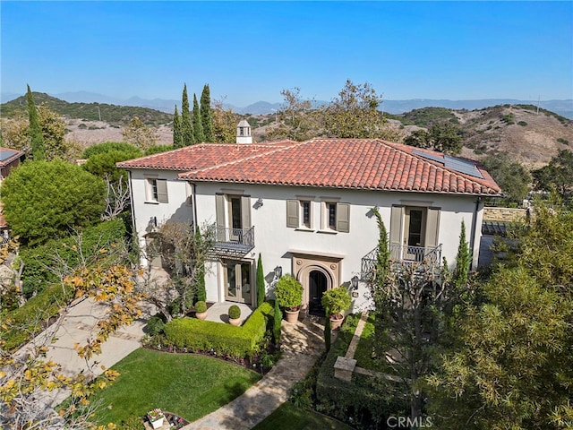 mediterranean / spanish house with solar panels, a balcony, a mountain view, and a front lawn