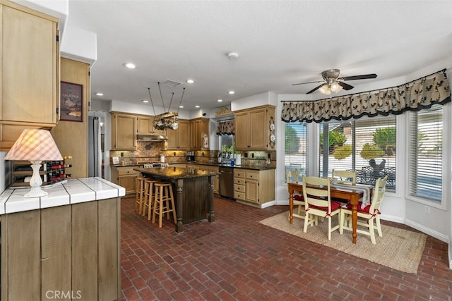 kitchen featuring tasteful backsplash, ceiling fan, appliances with stainless steel finishes, a kitchen breakfast bar, and a center island