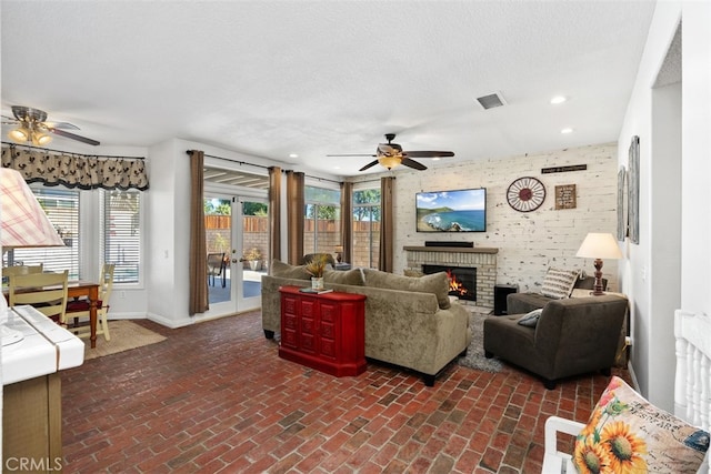 living room featuring french doors, ceiling fan, a textured ceiling, and a fireplace