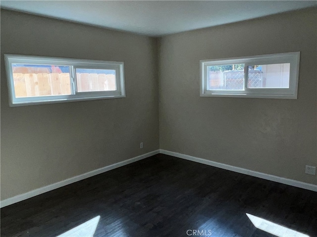 empty room with a wealth of natural light and dark hardwood / wood-style flooring