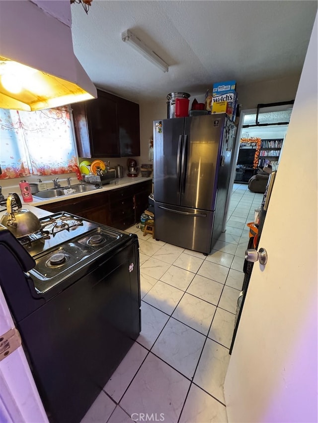 kitchen featuring black electric range oven, exhaust hood, sink, light tile patterned flooring, and stainless steel refrigerator