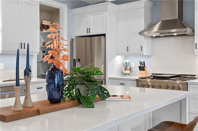 kitchen with wall chimney range hood, a breakfast bar, white cabinets, and stainless steel appliances