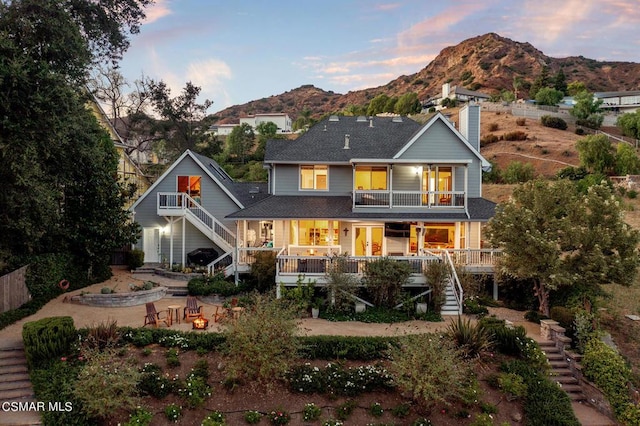 back house at dusk with a mountain view, a balcony, and covered porch