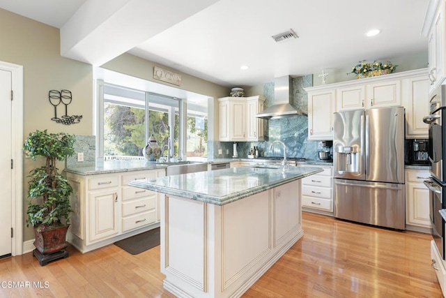 kitchen with light stone countertops, stainless steel appliances, wall chimney range hood, and light hardwood / wood-style floors