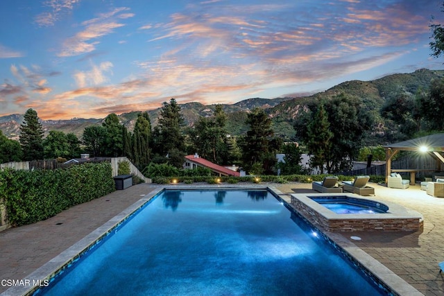 pool at dusk with a gazebo, a mountain view, an in ground hot tub, and a patio