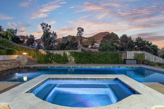 pool at dusk featuring an in ground hot tub