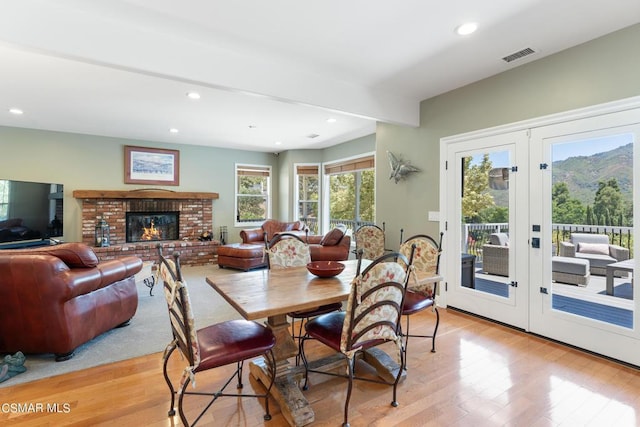 dining area with beamed ceiling, light wood-type flooring, french doors, and a brick fireplace