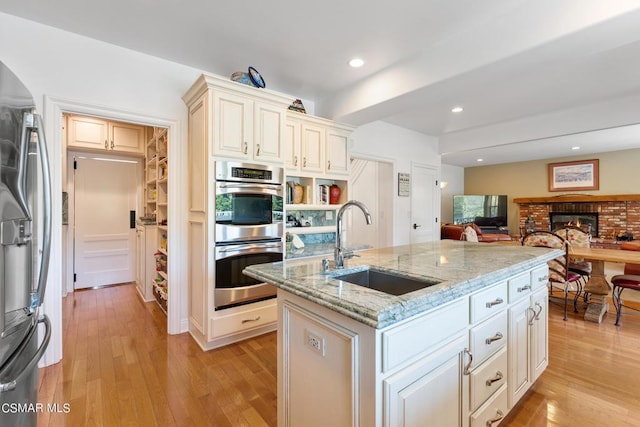 kitchen featuring light stone countertops, sink, stainless steel appliances, a kitchen island with sink, and light wood-type flooring