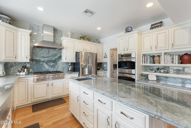 kitchen with sink, wall chimney exhaust hood, stainless steel appliances, light stone counters, and light wood-type flooring