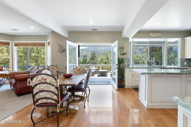 dining area with beam ceiling, sink, and light hardwood / wood-style flooring