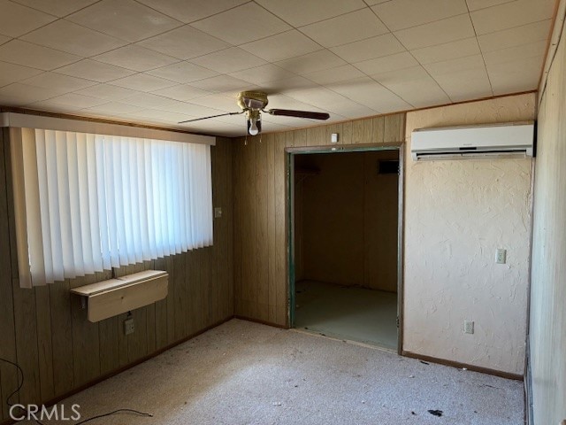 unfurnished bedroom featuring a closet, ceiling fan, a wall mounted AC, and wooden walls