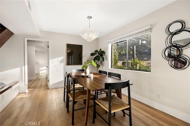 dining area with light wood-type flooring and an inviting chandelier