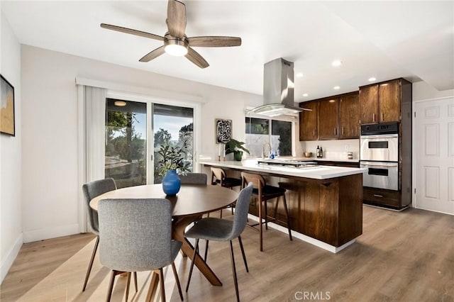 kitchen with light hardwood / wood-style flooring, ceiling fan, appliances with stainless steel finishes, kitchen peninsula, and island exhaust hood