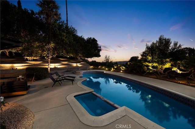 pool at dusk with a patio area and an in ground hot tub