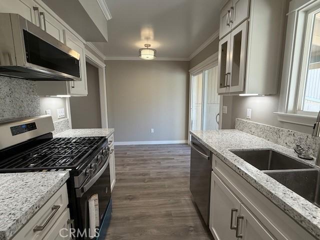 kitchen featuring ornamental molding, baseboards, a sink, dark wood finished floors, and appliances with stainless steel finishes