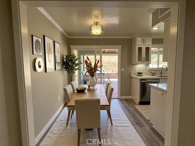 dining area with baseboards, ornamental molding, and light wood-type flooring