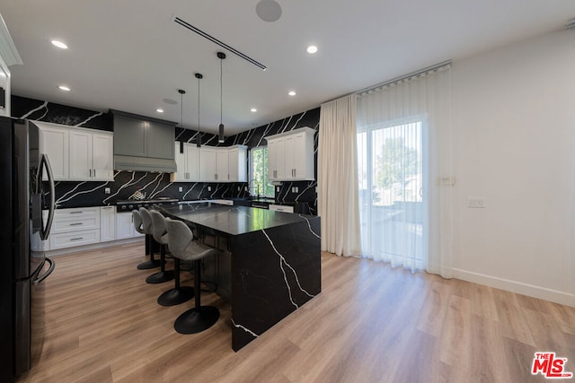 kitchen with hanging light fixtures, light wood-type flooring, stainless steel fridge, and a center island