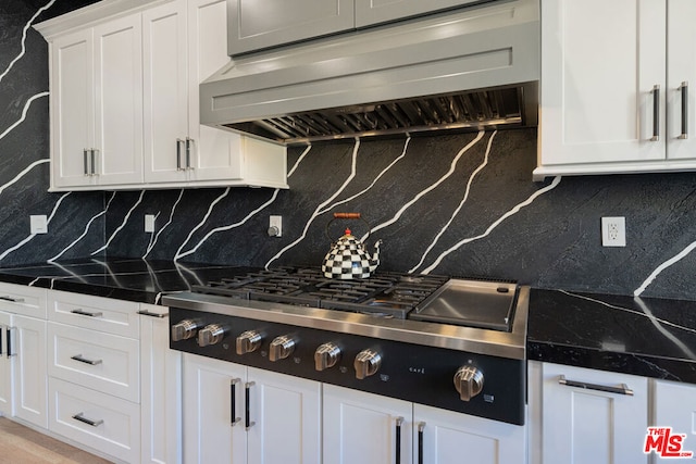 kitchen with exhaust hood, backsplash, stainless steel gas cooktop, dark stone counters, and white cabinets