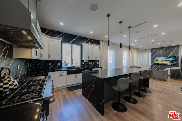 kitchen featuring exhaust hood, hanging light fixtures, a kitchen island, white cabinets, and sink