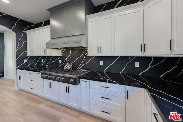 kitchen featuring decorative backsplash, stainless steel gas cooktop, dark stone counters, range hood, and white cabinets