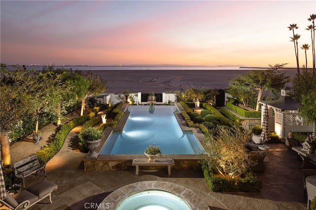 pool at dusk featuring an in ground hot tub and a patio area