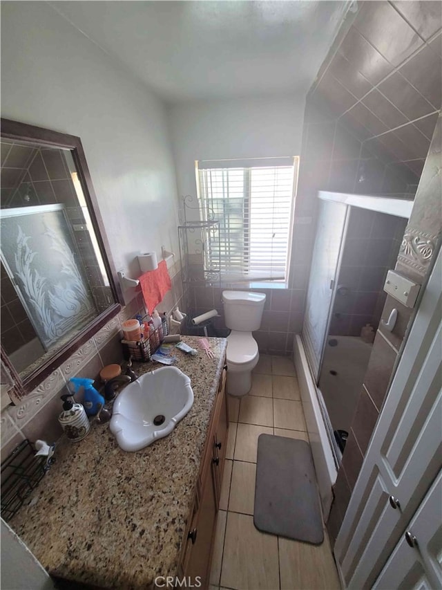 bathroom featuring tile walls, toilet, a shower with shower door, vanity, and tile patterned floors