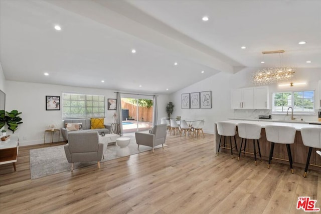 living room featuring a notable chandelier, sink, light hardwood / wood-style flooring, and vaulted ceiling with beams