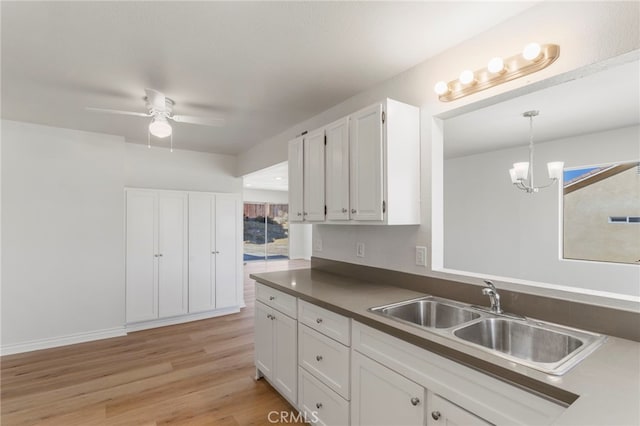 kitchen with white cabinetry, sink, light hardwood / wood-style flooring, pendant lighting, and ceiling fan with notable chandelier