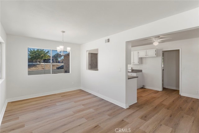 unfurnished dining area featuring ceiling fan with notable chandelier and light wood-type flooring