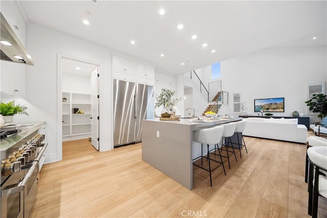 kitchen with a breakfast bar, a kitchen island with sink, white cabinets, appliances with stainless steel finishes, and light hardwood / wood-style floors