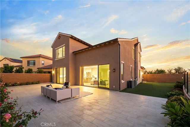 back house at dusk with outdoor lounge area, a patio area, a yard, and central air condition unit