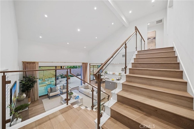 stairs featuring beam ceiling, high vaulted ceiling, and wood-type flooring