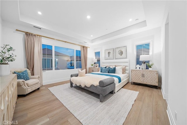 bedroom with light wood-type flooring and a tray ceiling