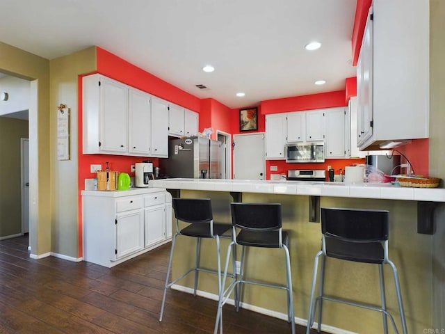 kitchen featuring a breakfast bar, tile counters, white cabinets, and stainless steel appliances