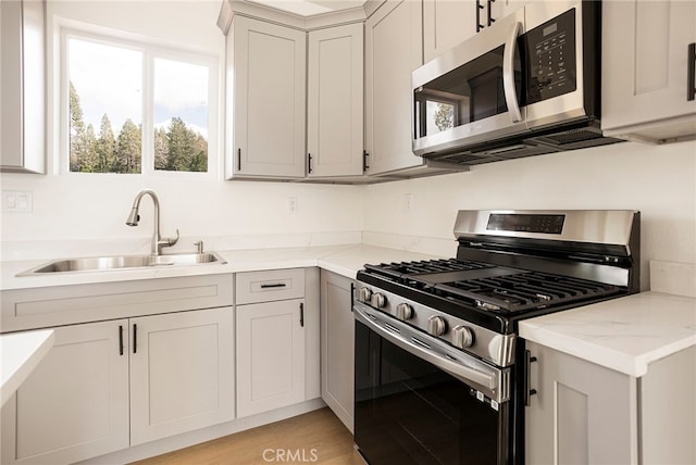 kitchen with sink, light stone countertops, stainless steel appliances, and light wood-type flooring