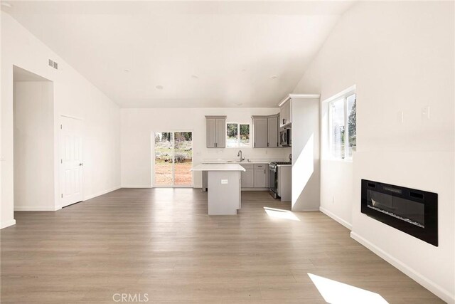 13990 Pineland Cir, Magalia, CA 95954 - unfurnished living room with vaulted ceiling, light wood-style flooring, baseboards, a sink, and a glass covered fireplace