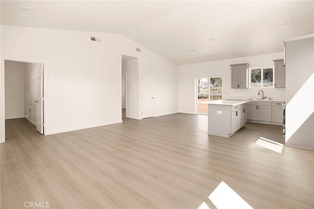 kitchen featuring kitchen peninsula, vaulted ceiling, light hardwood / wood-style flooring, gray cabinetry, and sink
