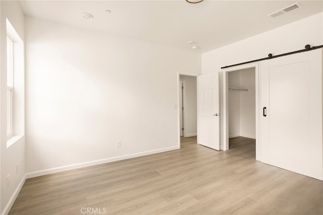 unfurnished bedroom featuring light hardwood / wood-style floors, a closet, and a barn door