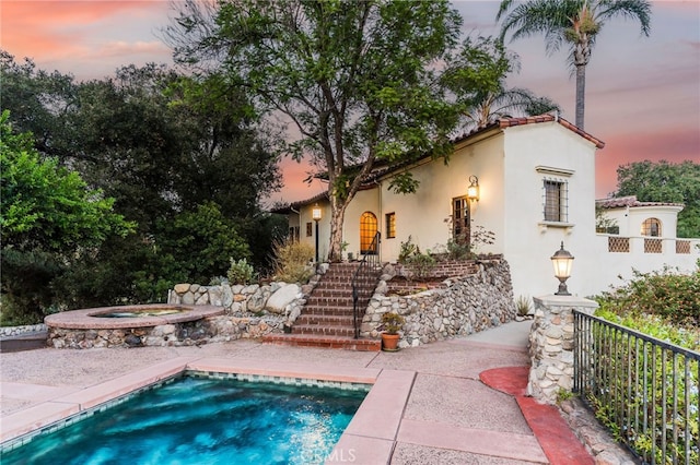 back house at dusk with a pool with hot tub