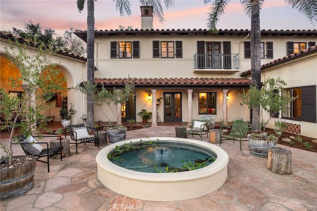 back house at dusk featuring a balcony and a patio