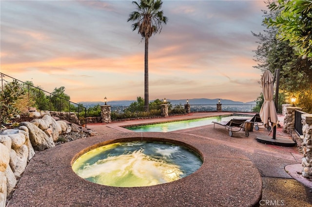 pool at dusk with an in ground hot tub, a mountain view, and a patio area