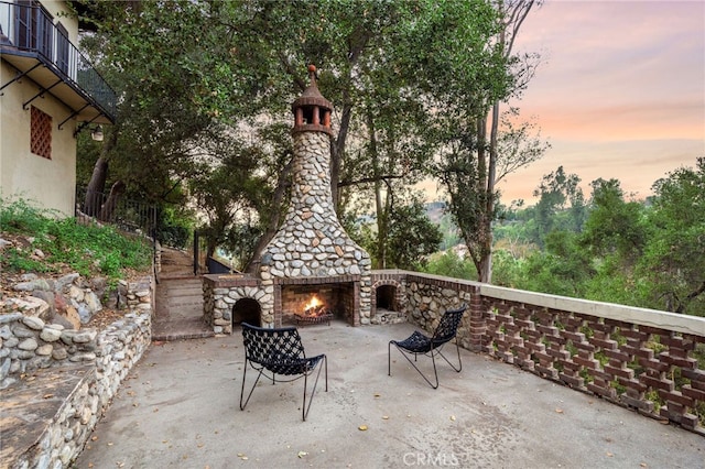 patio terrace at dusk featuring an outdoor stone fireplace