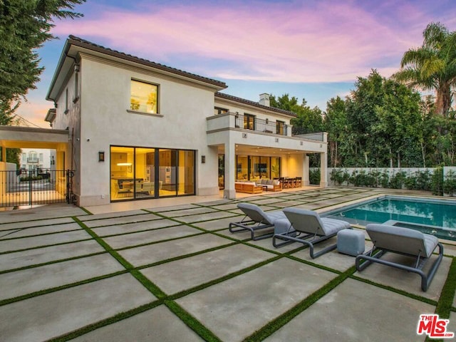 back house at dusk featuring an outdoor hangout area, a balcony, a patio, and a fenced in pool